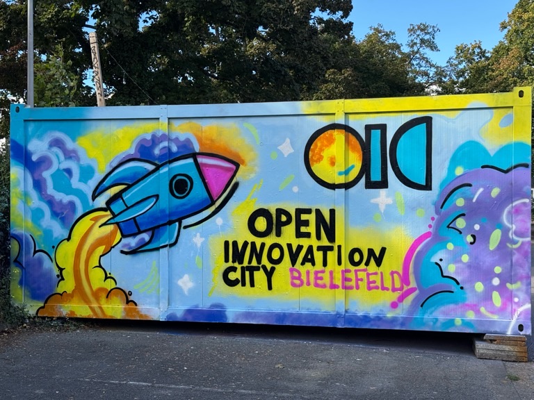 Ein Graffiti-Bild ist auf einem Container zu sehen. Darauf sieht man eine Rakete, die ins All fliegt. Daneben steht OIC Open Innovation City Bielefeld